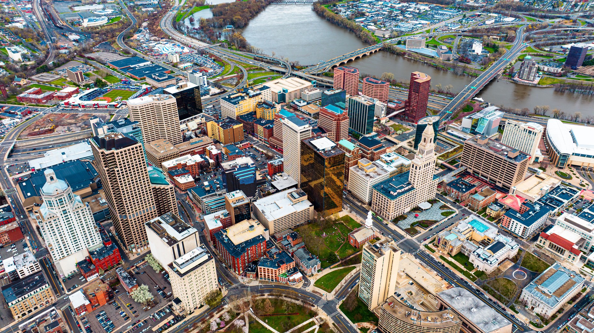 Downtown of beautiful modern Hartford, Connecticut, the USA at daytime. View on the river floating through the city at backdrop. Aerial perspective.